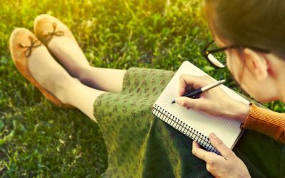 girl with pen writing on notebook on grass outside